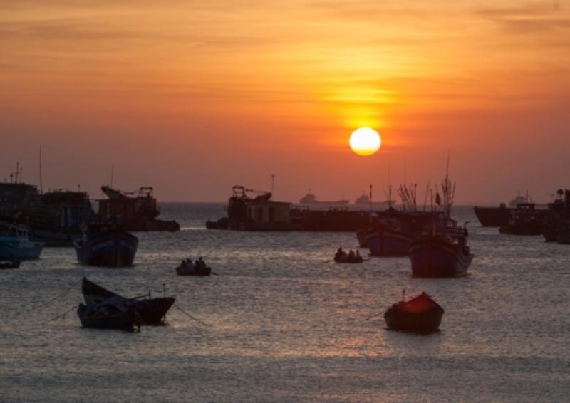 Một du khách đang thư giãn tại ban công của khách sạn bãi trước Vũng Tàu, ngắm nhìn khung cảnh hoàng hôn rực rỡ trên biển Bãi Trước, với những chiếc thuyền neo đậu và đường phố ven biển lung linh ánh đèn.